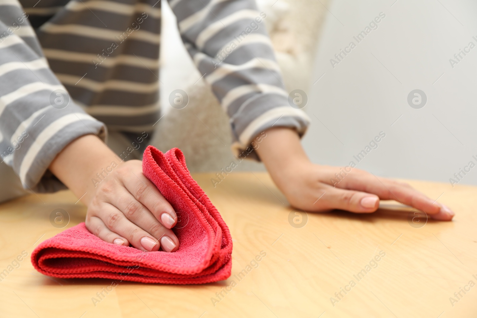 Photo of Woman wiping coffee table with rag indoors, closeup