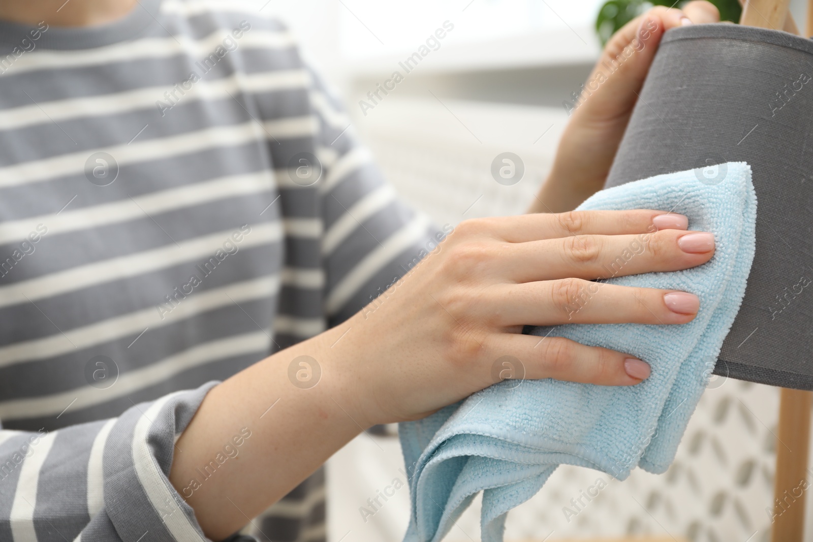 Photo of Woman wiping lamp with rag indoors, closeup