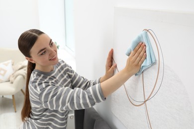 Photo of Beautiful young woman wiping picture with rag at home