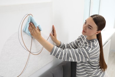 Beautiful young woman wiping picture with rag at home