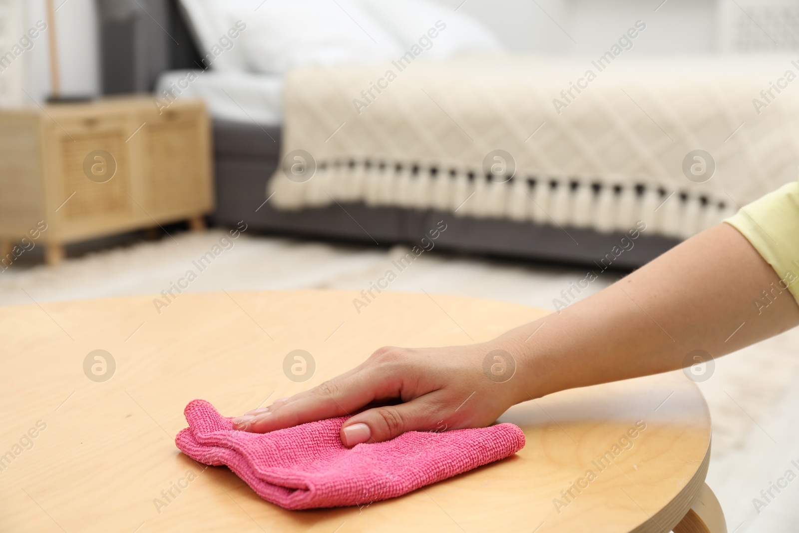 Photo of Woman wiping coffee table with rag indoors, closeup