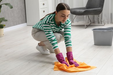 Beautiful young woman cleaning floor with rag at home