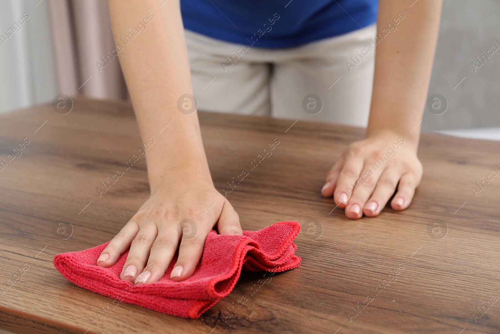 Photo of Woman wiping wooden table with rag indoors, closeup