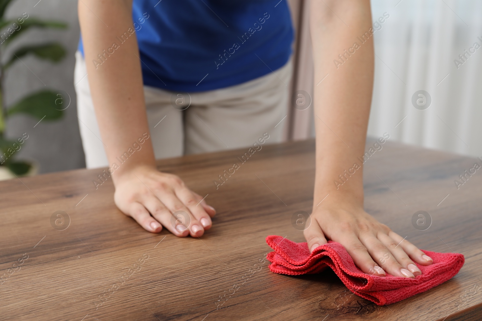 Photo of Woman wiping wooden table with rag indoors, closeup