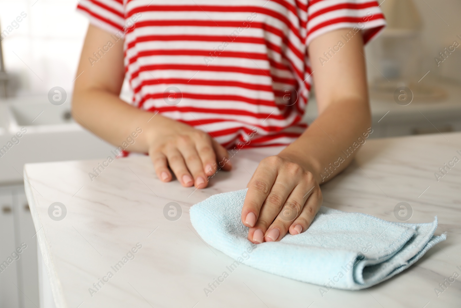 Photo of Woman wiping white marble countertop with rag in kitchen, closeup