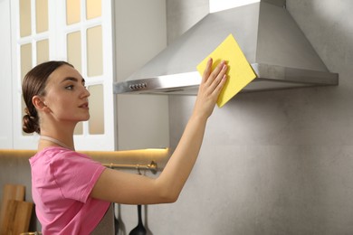 Photo of Beautiful young woman cleaning kitchen hood with napkin at home