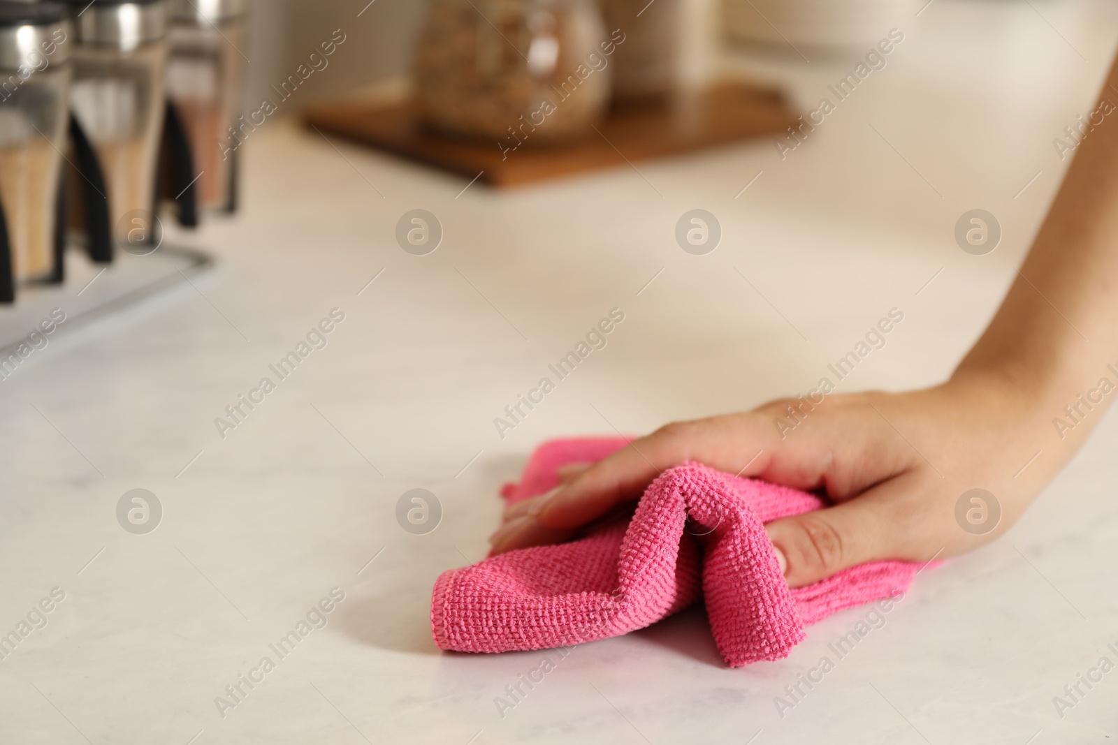 Photo of Woman wiping white marble countertop with rag indoors, closeup