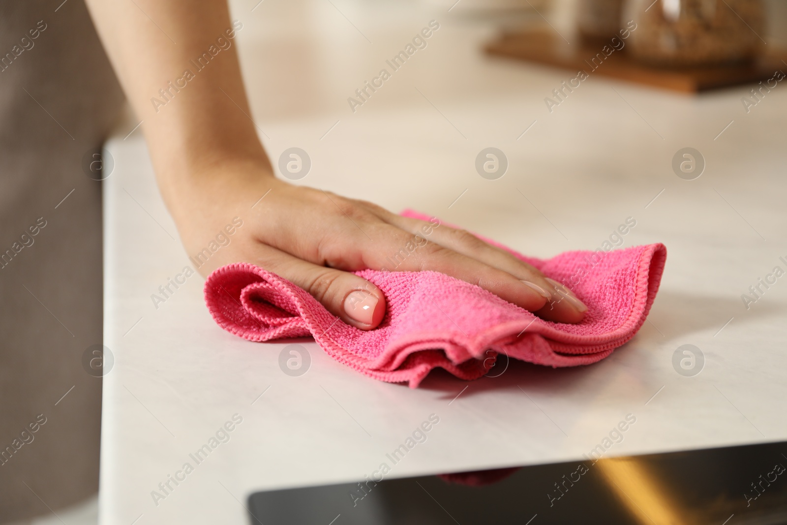 Photo of Woman wiping white marble countertop with rag indoors, closeup