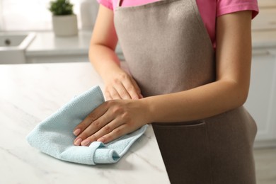 Woman wiping white marble countertop with rag in kitchen, closeup