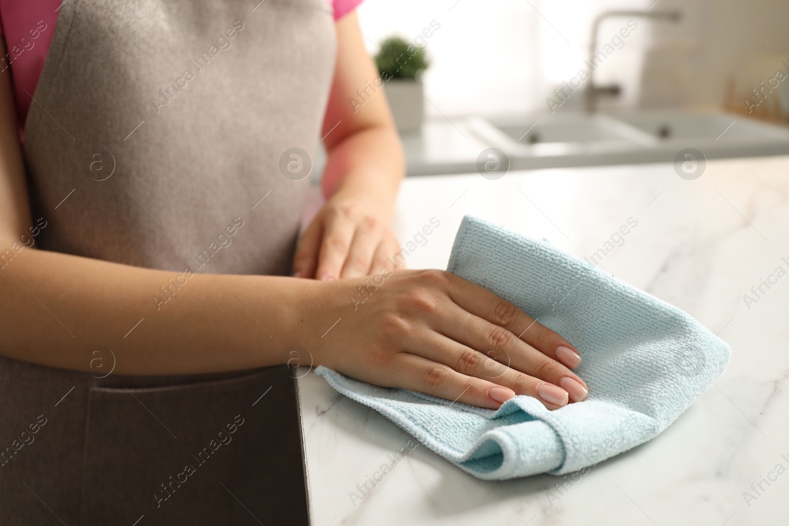 Photo of Woman wiping white marble countertop with rag in kitchen, closeup