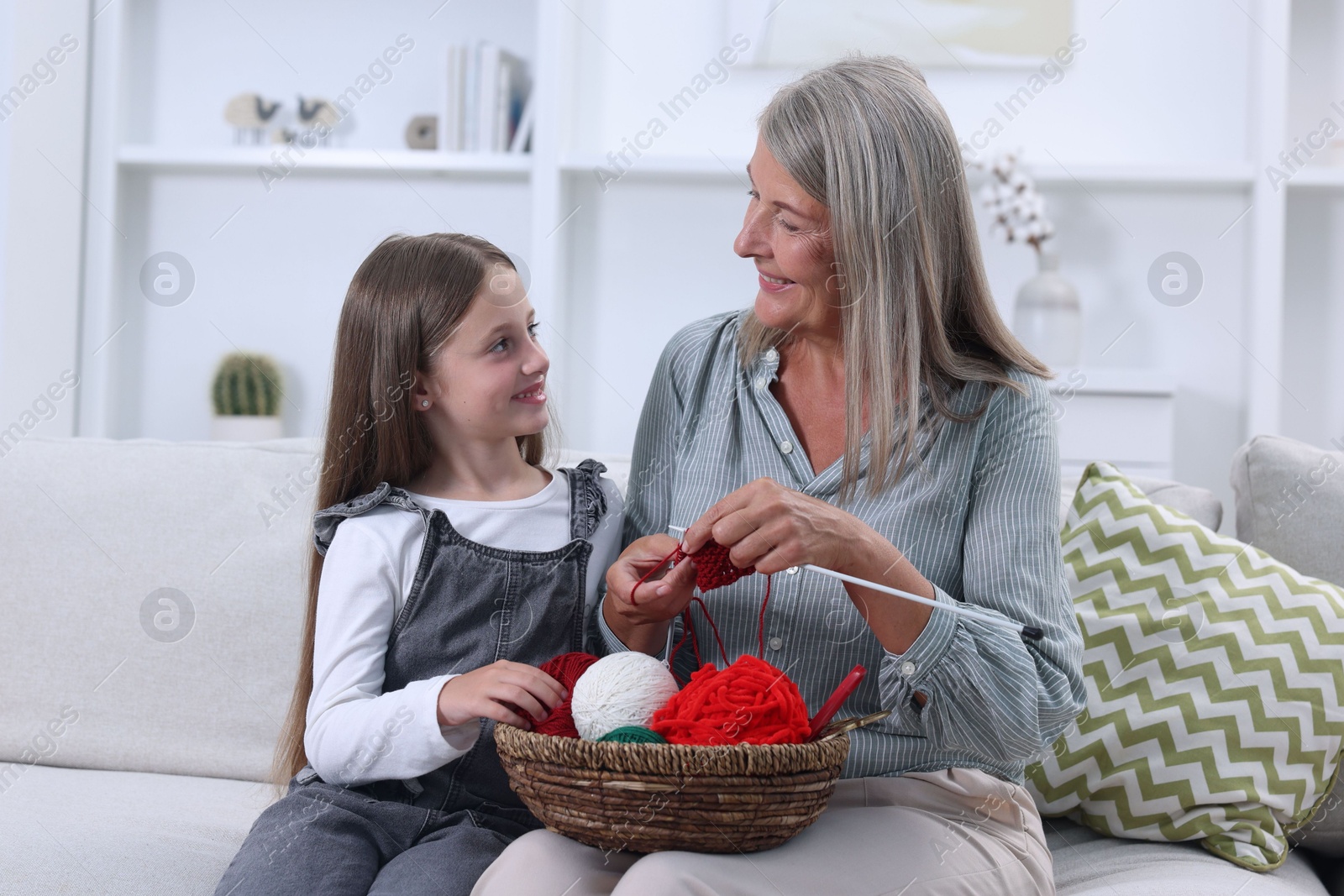 Photo of Smiling grandmother teaching her granddaughter to knit on sofa at home