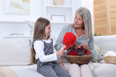 Grandmother teaching her granddaughter to knit on sofa at home