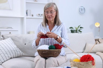 Photo of Woman with basket of yarn knitting on sofa at home