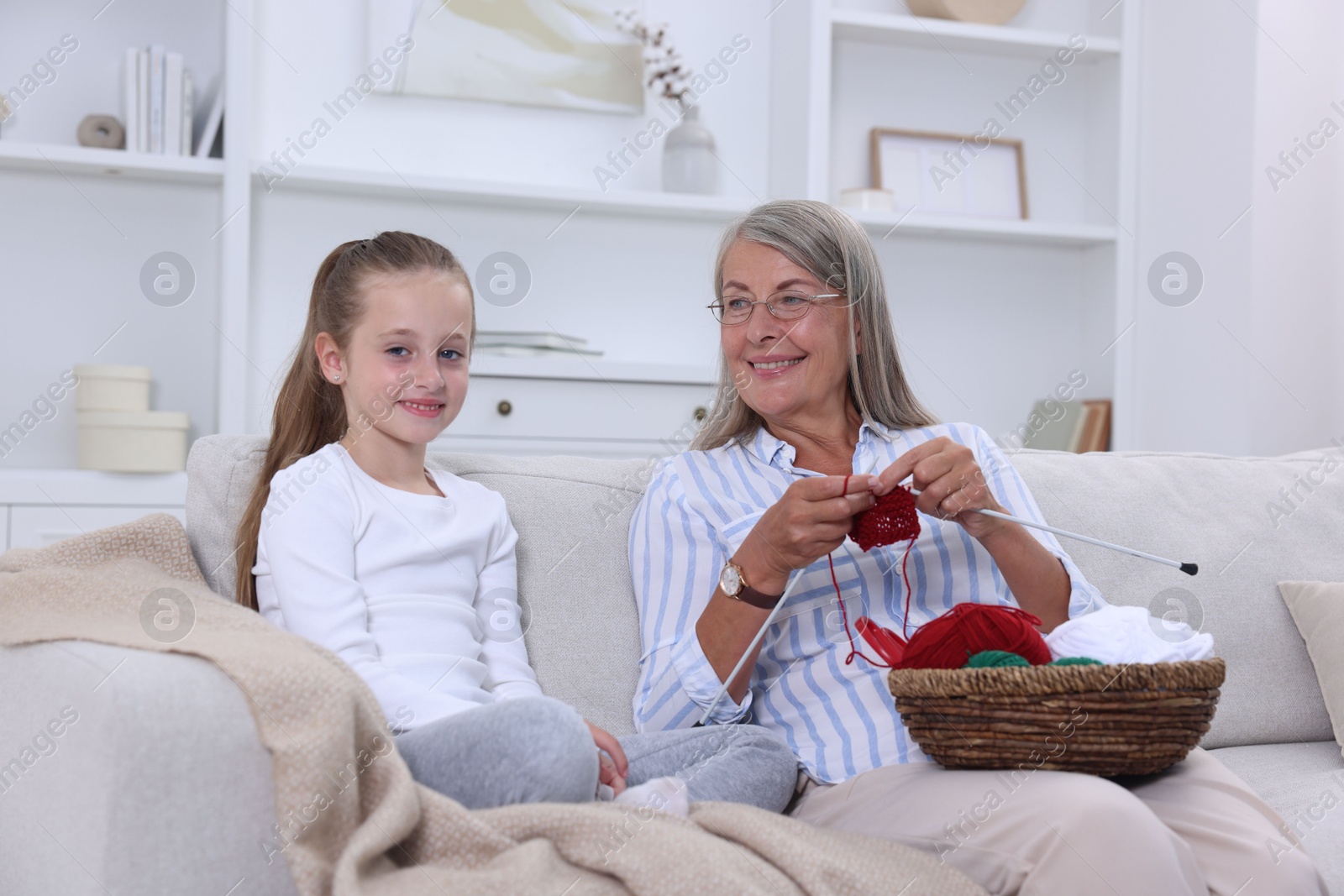 Photo of Smiling grandmother teaching her granddaughter to knit on sofa at home