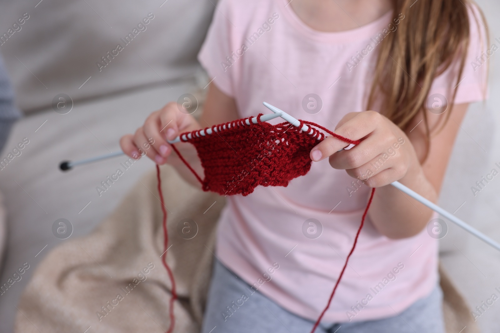 Photo of Little girl learning to knit on sofa, closeup