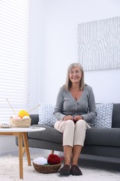 Smiling senior woman with skeins of yarn on sofa at home