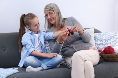 Grandmother teaching her granddaughter to knit on sofa at home