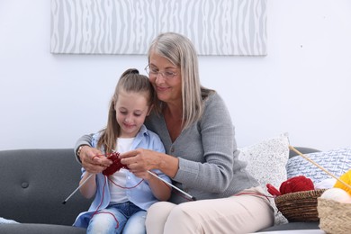 Grandmother teaching her granddaughter to knit on sofa at home