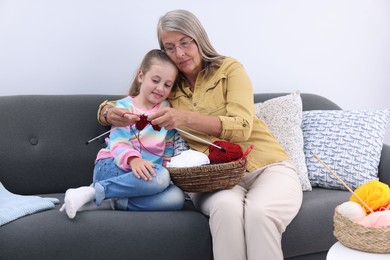 Photo of Grandmother teaching her granddaughter to knit on sofa at home