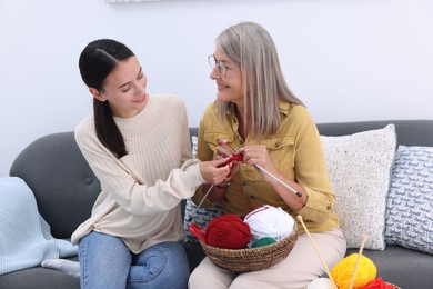 Photo of Smiling daughter observing her mother knitting on sofa at home