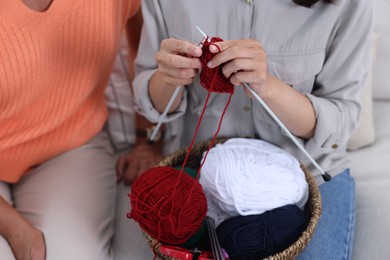 Photo of Daughter learning to knit near her grandmother on sofa, closeup