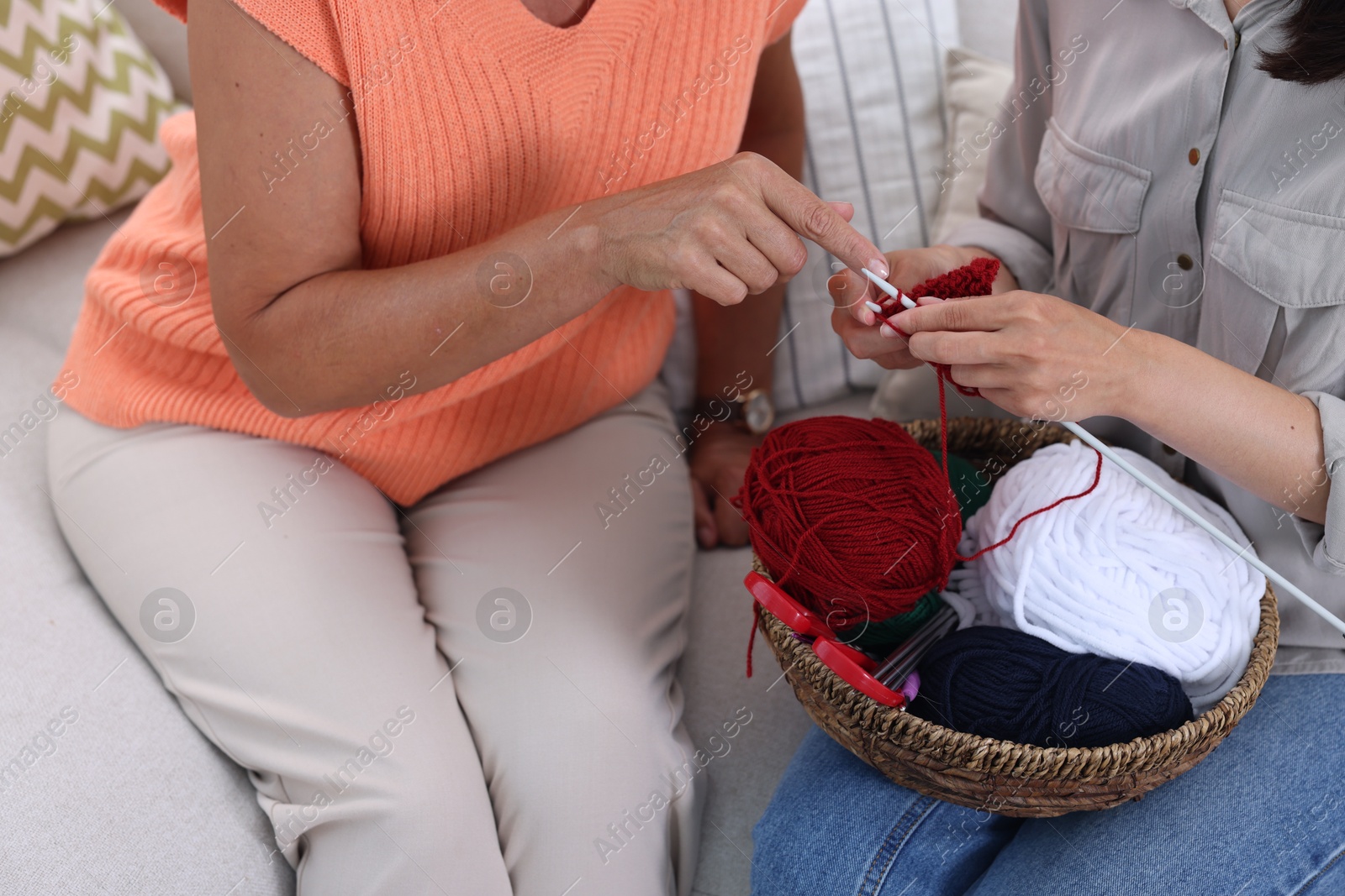 Photo of Mother teaching her daughter how to knit on sofa, closeup