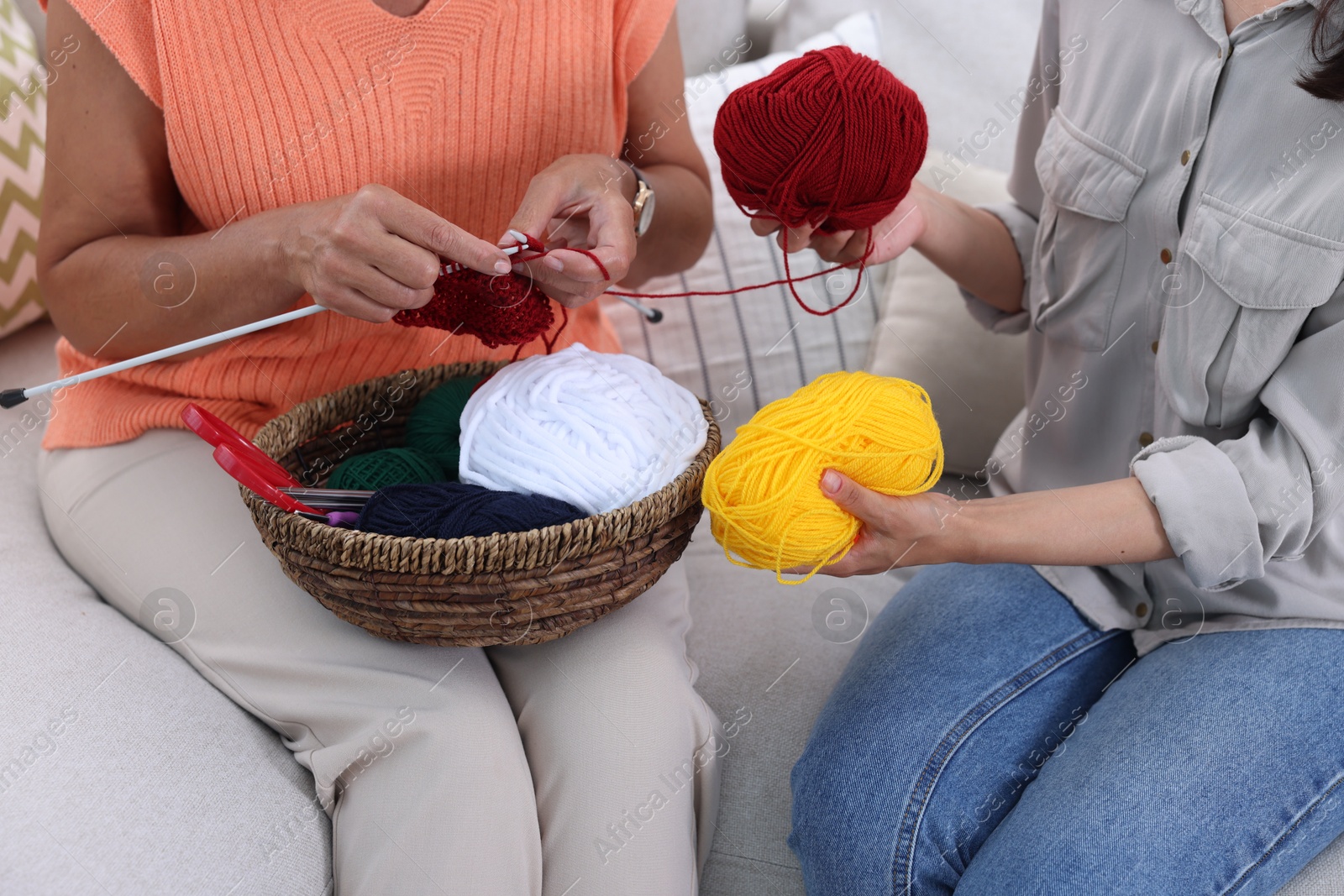 Photo of Mother knitting while her daughter holding yarns on sofa, closeup