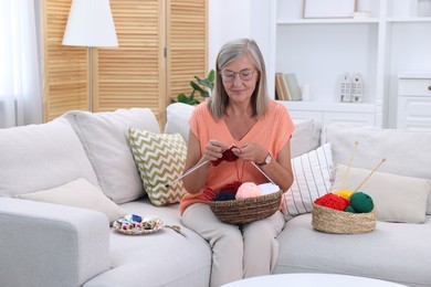 Photo of Beautiful senior woman knitting on sofa at home