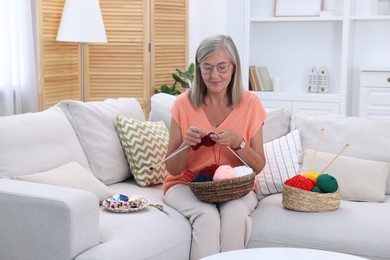 Beautiful senior woman knitting on sofa at home