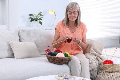 Beautiful senior woman knitting on sofa at home