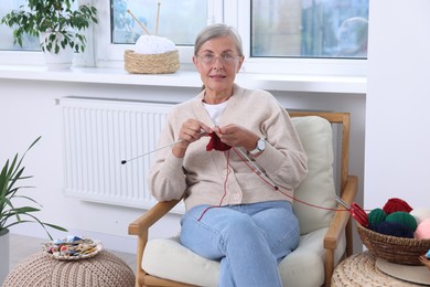 Beautiful senior woman knitting on armchair at home