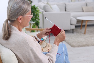 Senior woman with knitting needles looking at pattern at home