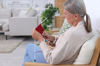 Senior woman with knitting needles looking at pattern at home