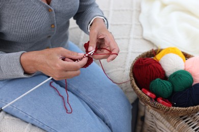 Photo of Woman with basket of yarn knitting at home, closeup