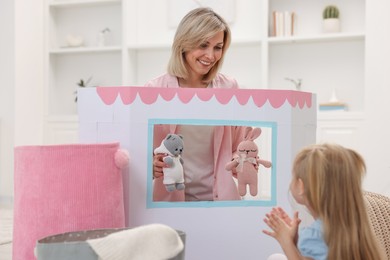 Photo of Puppet theatre. Smiling mother performing show with toys to her daughter at home