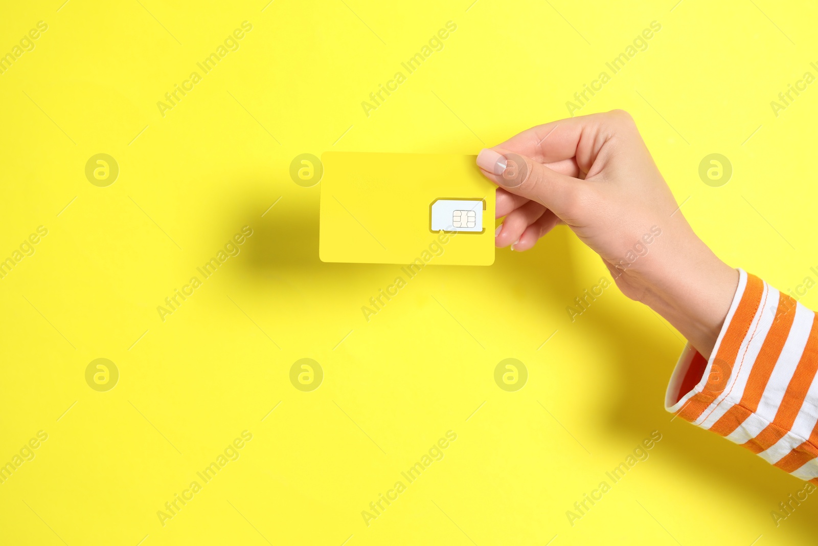 Photo of Woman holding SIM card on yellow background, closeup