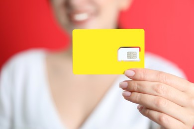 Photo of Woman holding SIM card on red background, closeup