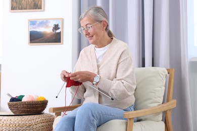 Smiling senior woman knitting on armchair at home