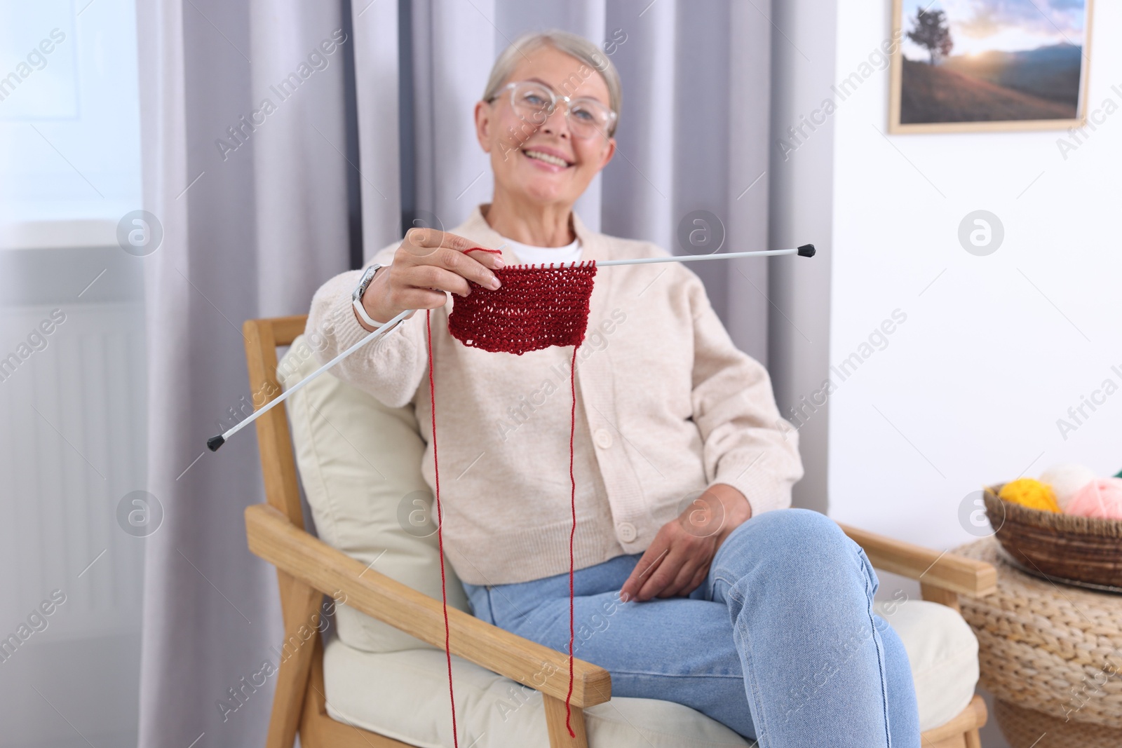 Photo of Smiling senior woman showing knitting needles on armchair at home