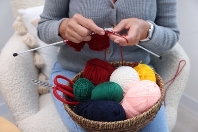 Photo of Woman with basket of yarn knitting at home, closeup