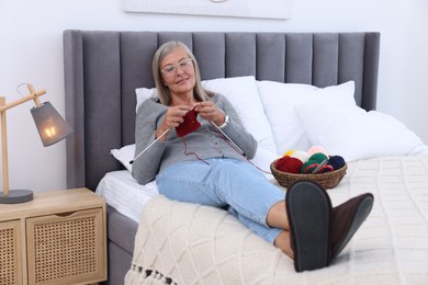 Smiling senior woman knitting on bed at home