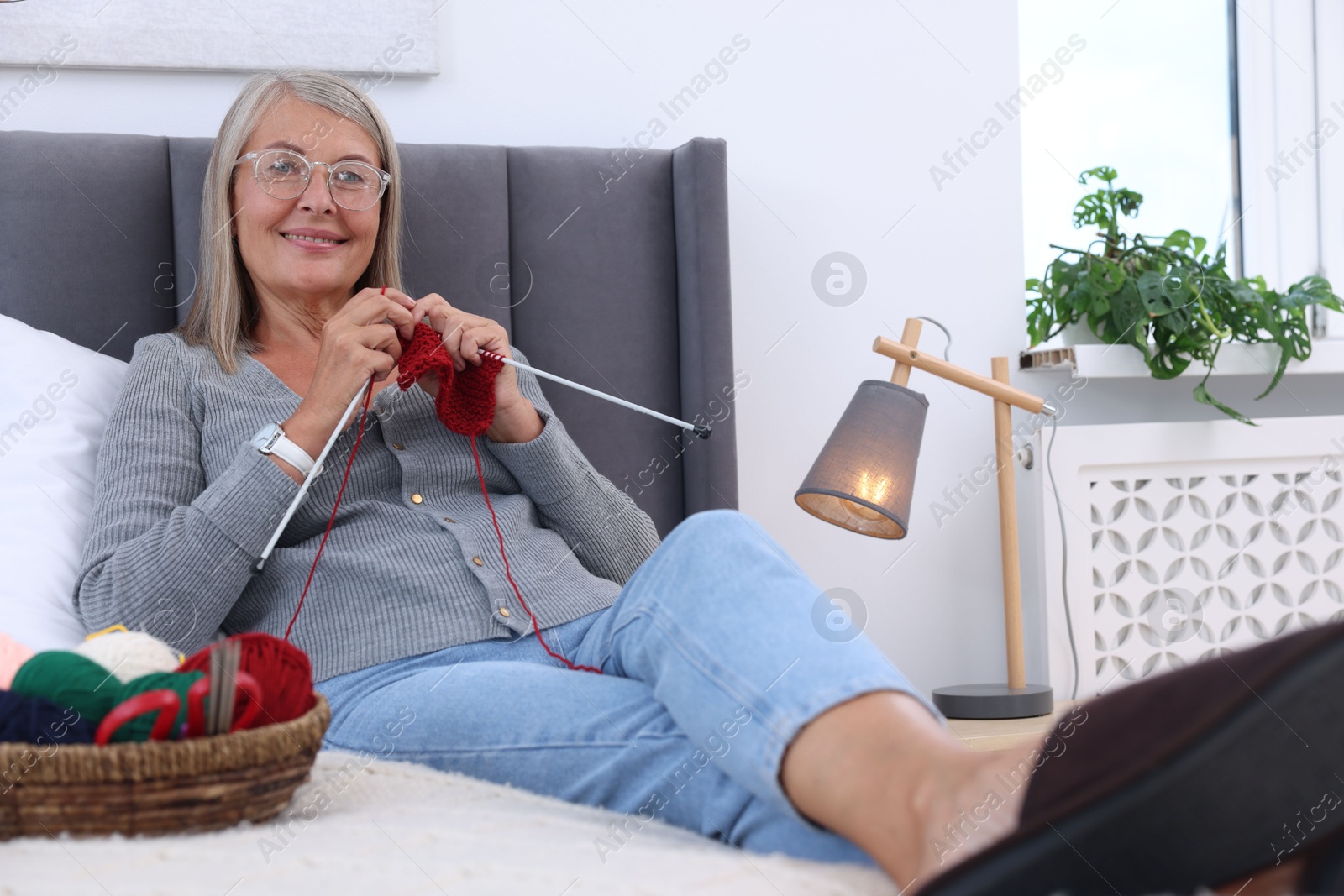 Photo of Smiling senior woman knitting on bed at home