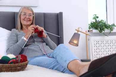 Smiling senior woman knitting on bed at home