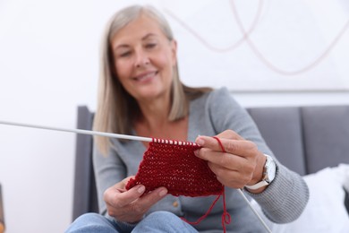 Photo of Smiling senior woman with knitting needles looking at pattern at home, selective focus