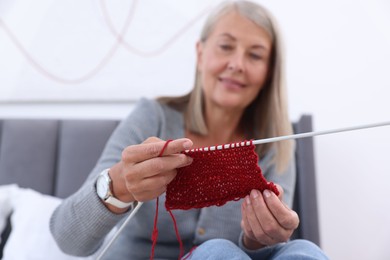 Photo of Smiling senior woman with knitting needles looking at pattern at home, selective focus