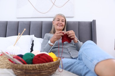 Smiling senior woman knitting on bed at home