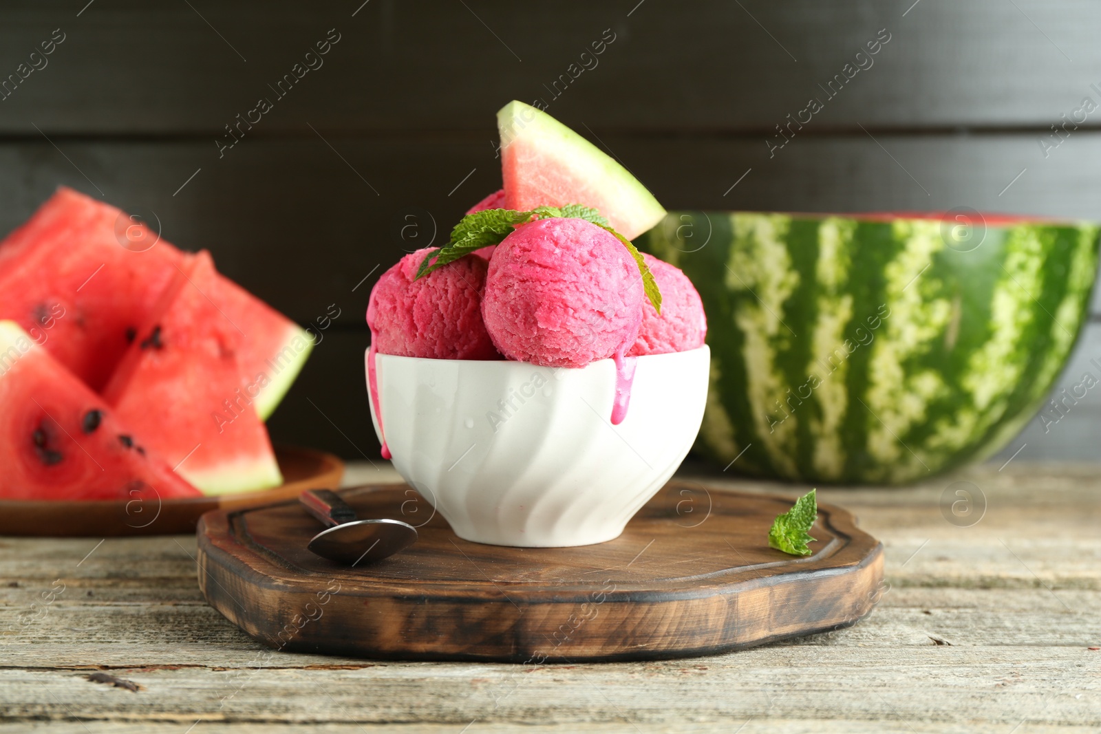 Photo of Scoops of tasty watermelon sorbet in bowl, fresh fruit, mint and spoon on wooden table