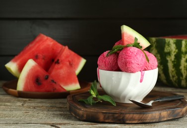 Photo of Scoops of tasty watermelon sorbet in bowl, fresh fruit, mint and spoon on wooden table