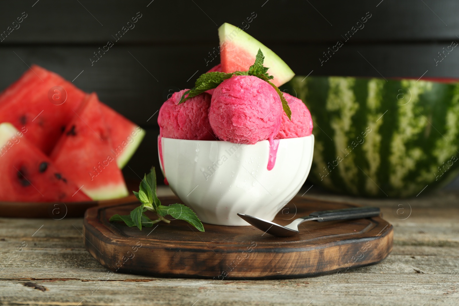 Photo of Scoops of tasty watermelon sorbet in bowl, fresh fruit, mint and spoon on wooden table