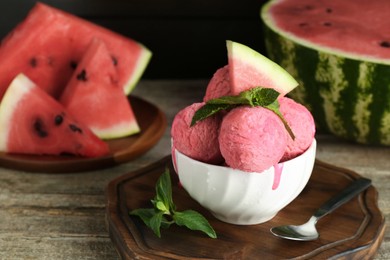 Photo of Scoops of tasty watermelon sorbet in bowl, fresh fruit, mint and spoon on wooden table